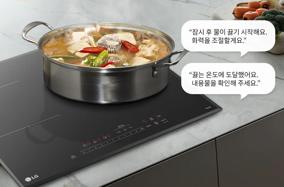 스테인리스 냄비에 국물이 담겨 있으며, 두부, 조개, 고추 등의 재료가 보입니다. 인덕션 위에 놓여 있고, 대화 상자에는 잠시 후 물이 끓기 시작해요. 화력을 조절할게요.와 끓는 온도에 도달했어요. 내용물을 확인해 주세요.라는 문구가 있습니다. 주위에는 야채가 놓여 있습니다.